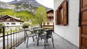 Un balcon avec une table et des chaises, donnant sur un paysage montagneux parsemé de bâtiments traditionnels en bois.