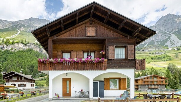 Un chalet en bois à deux étages, doté d’un balcon, d’une entrée en arc de cercle et offrant une vue sur la montagne.