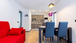 Un salon moderne avec un canapé rouge, un coin repas avec deux chaises bleues et une cuisine en arrière-plan.