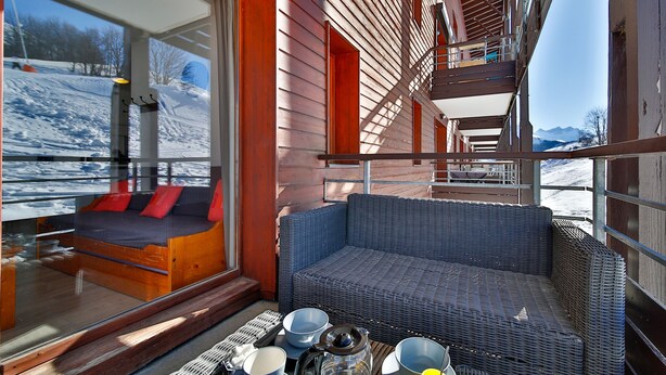 Een modern interieur met een rieten bank, een glazen deur naar een balkon en uitzicht op een besneeuwd landschap.