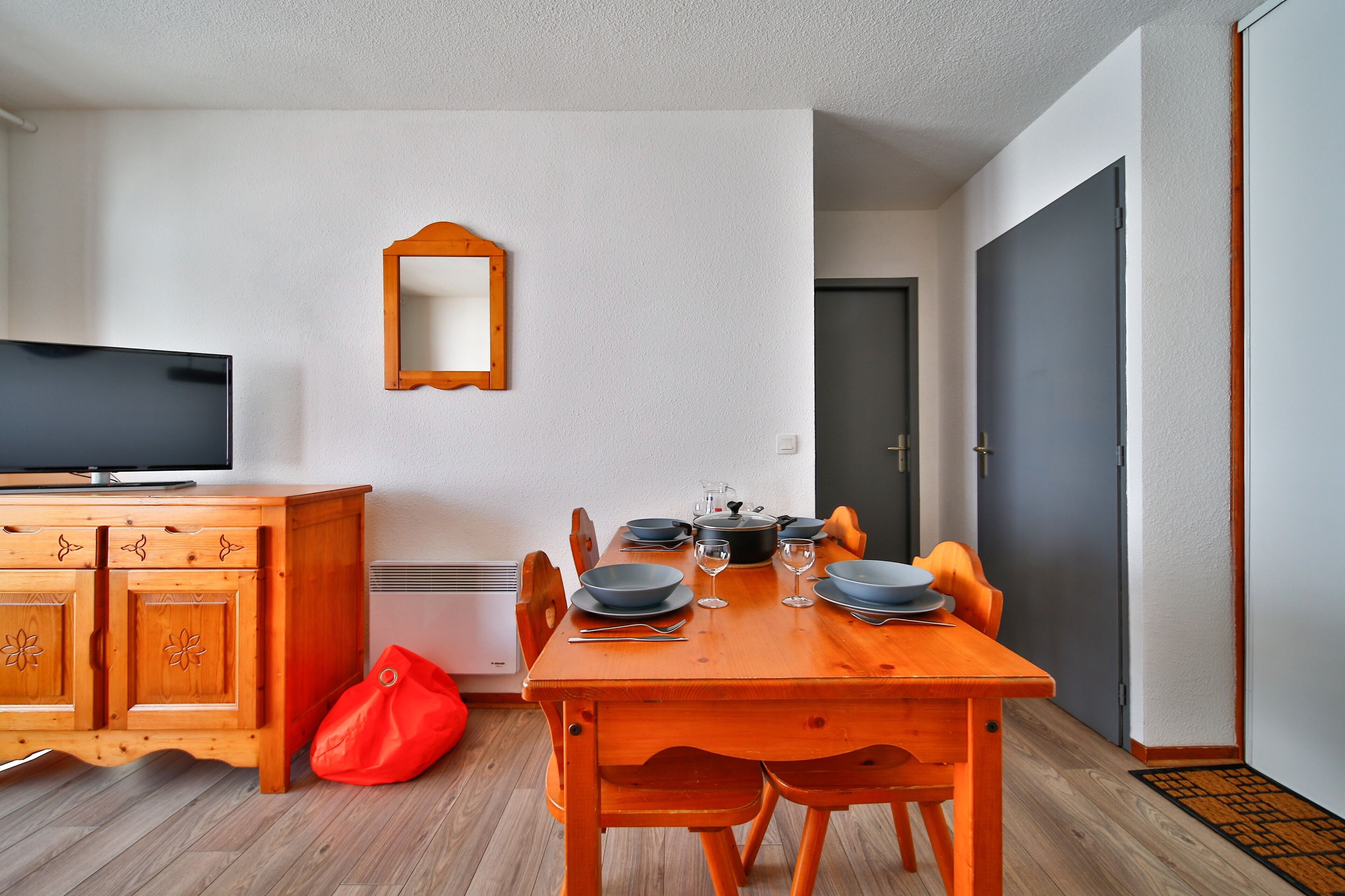 A compact living space with a dining table set for four, a television, and a mirror on the wall.