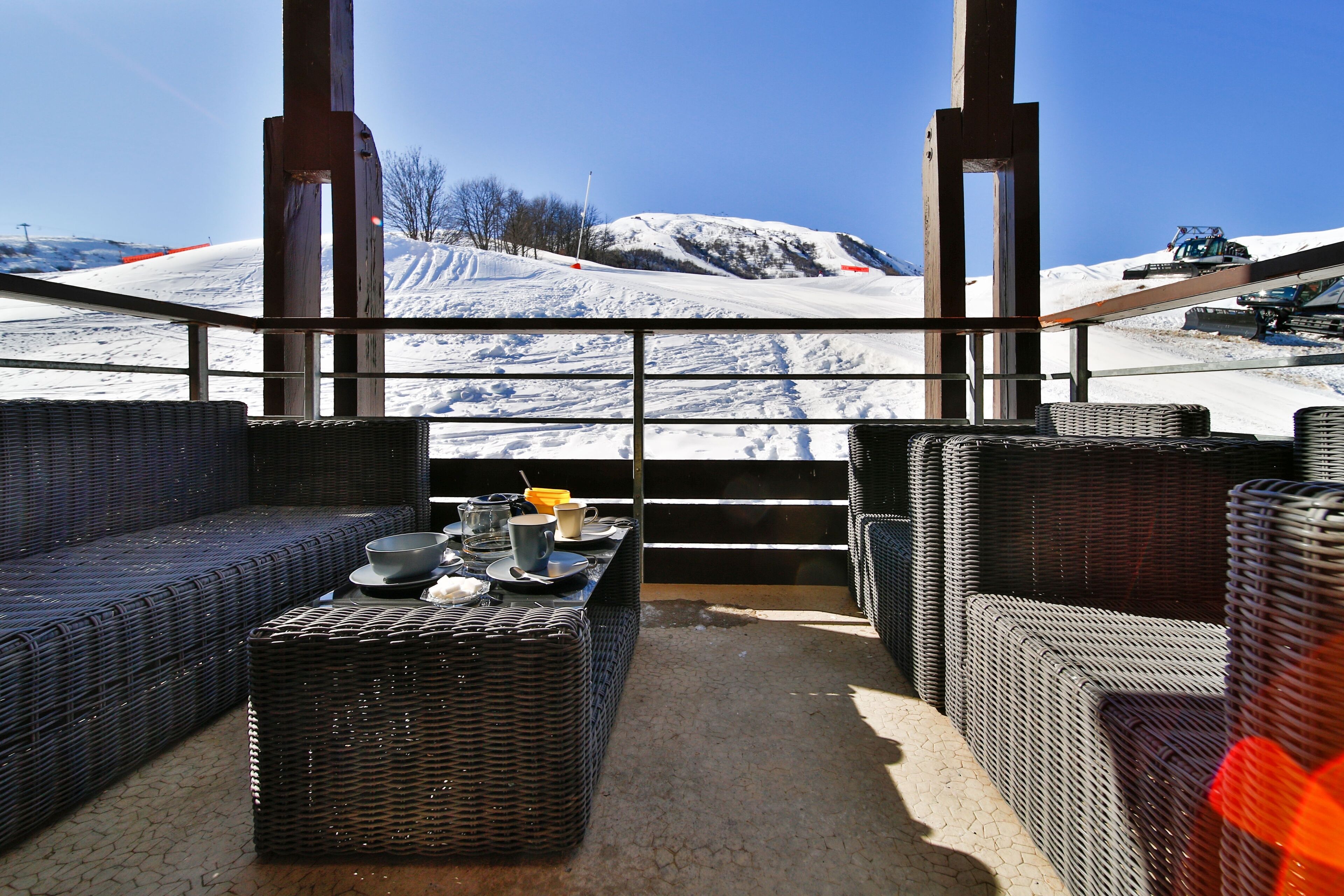 A room with wicker furniture and a table set for two, overlooking a snowy mountain.