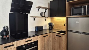 Een moderne keuken met zwarte en houten kastjes, een ingebouwde magnetron, een koffiezetapparaat en een broodrooster.
