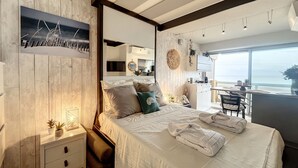 A modern bedroom with a large bed, a nightstand, a desk, and a view of the ocean. - Rêve de plage - Confortable appt pour 2 (Canet-en-Roussillon)