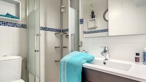 A modern bathroom with a glass-enclosed shower, a white toilet, a sink with a mirror, and a blue towel on the counter. - Rêve de plage - Confortable appt pour 2 (Canet-en-Roussillon)