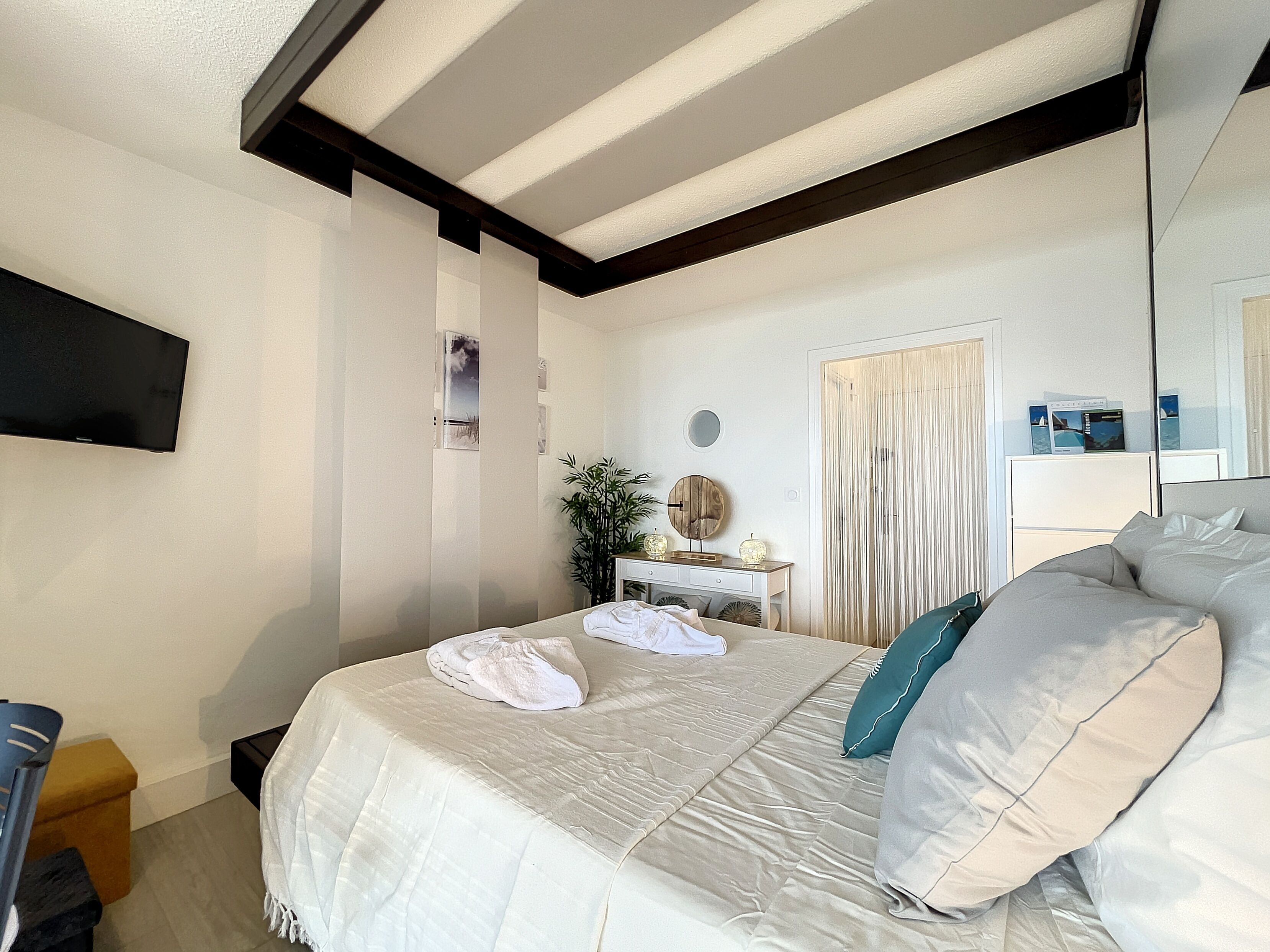 Une chambre à coucher comprenant un lit, une table de chevet, un miroir et un téléviseur fixé au mur.