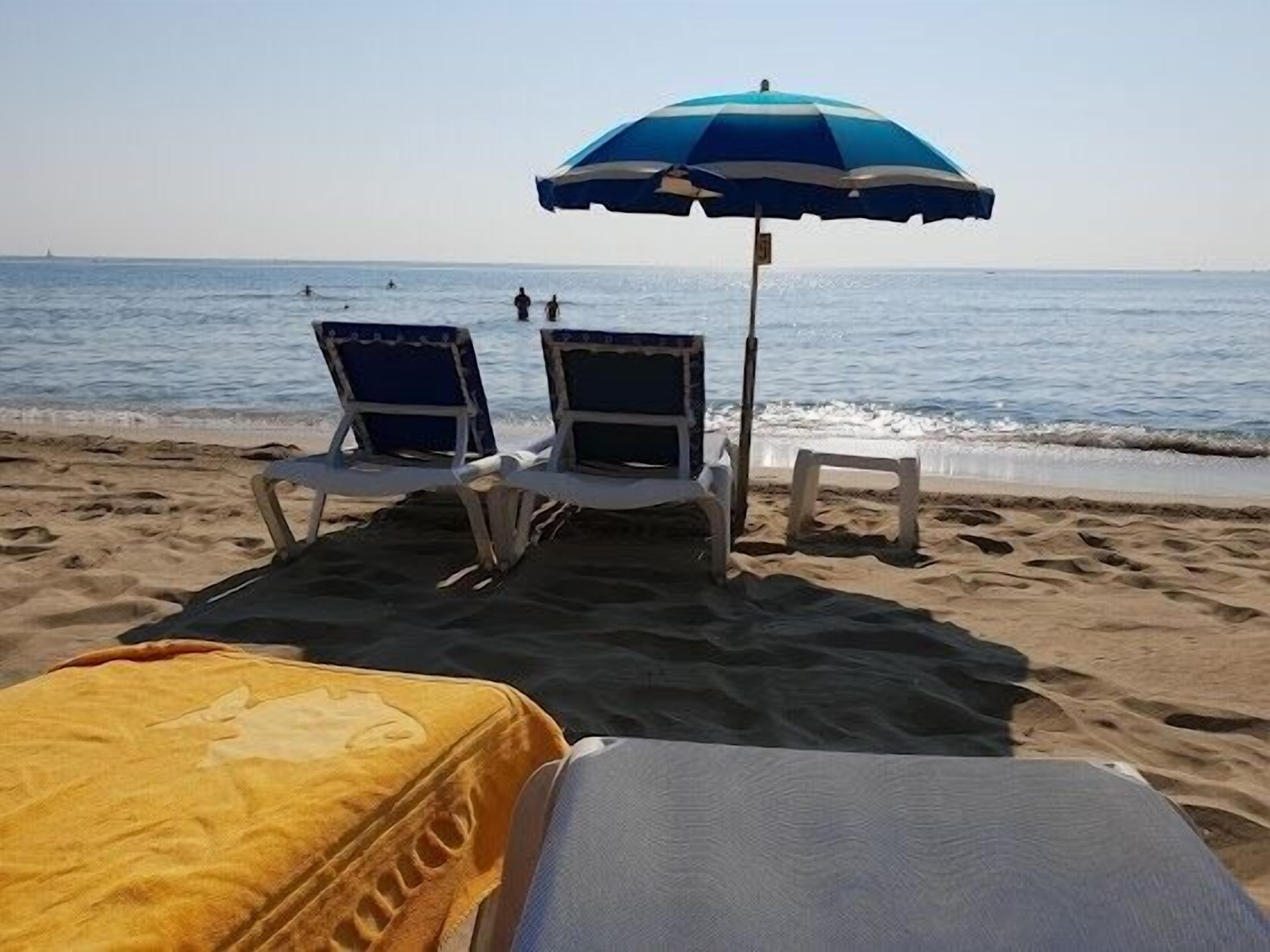 Een strand met twee strandstoelen en een blauw-witte parasol.