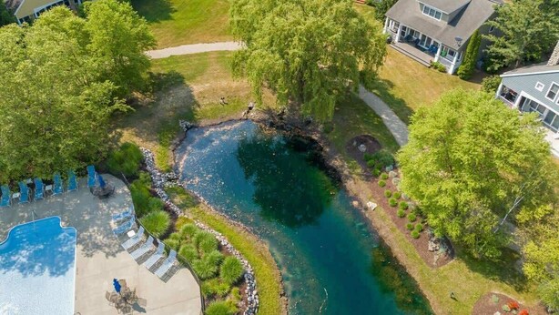 Vue aérienne d’un quartier résidentiel avec une piscine, une petite rivière et des maisons.