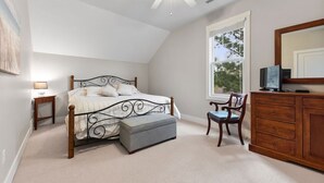 Une chambre à coucher comprenant un lit, une commode, une chaise, une fenêtre et un ventilateur de plafond.