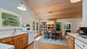 A kitchen with wooden cabinets, a white microwave, and a dining area with chairs and a table.