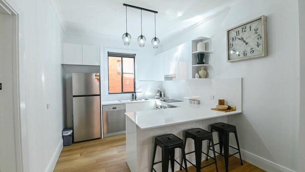 Una cocina moderna con una isla central, electrodomésticos de acero inoxidable y taburetes negros.