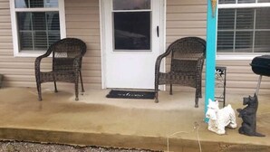 Entrada de una casa con dos sillas de mimbre y una estatua de perro.