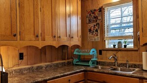 Una cocina con armarios de madera, encimera de granito, ventana con persianas y un escurreplatos verde.