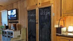 Una habitación acogedora con armarios de madera, un televisor, una pizarra con ‘Welcome’ y ‘Frankies Cottage’ escritos, y un sillón cómodo.