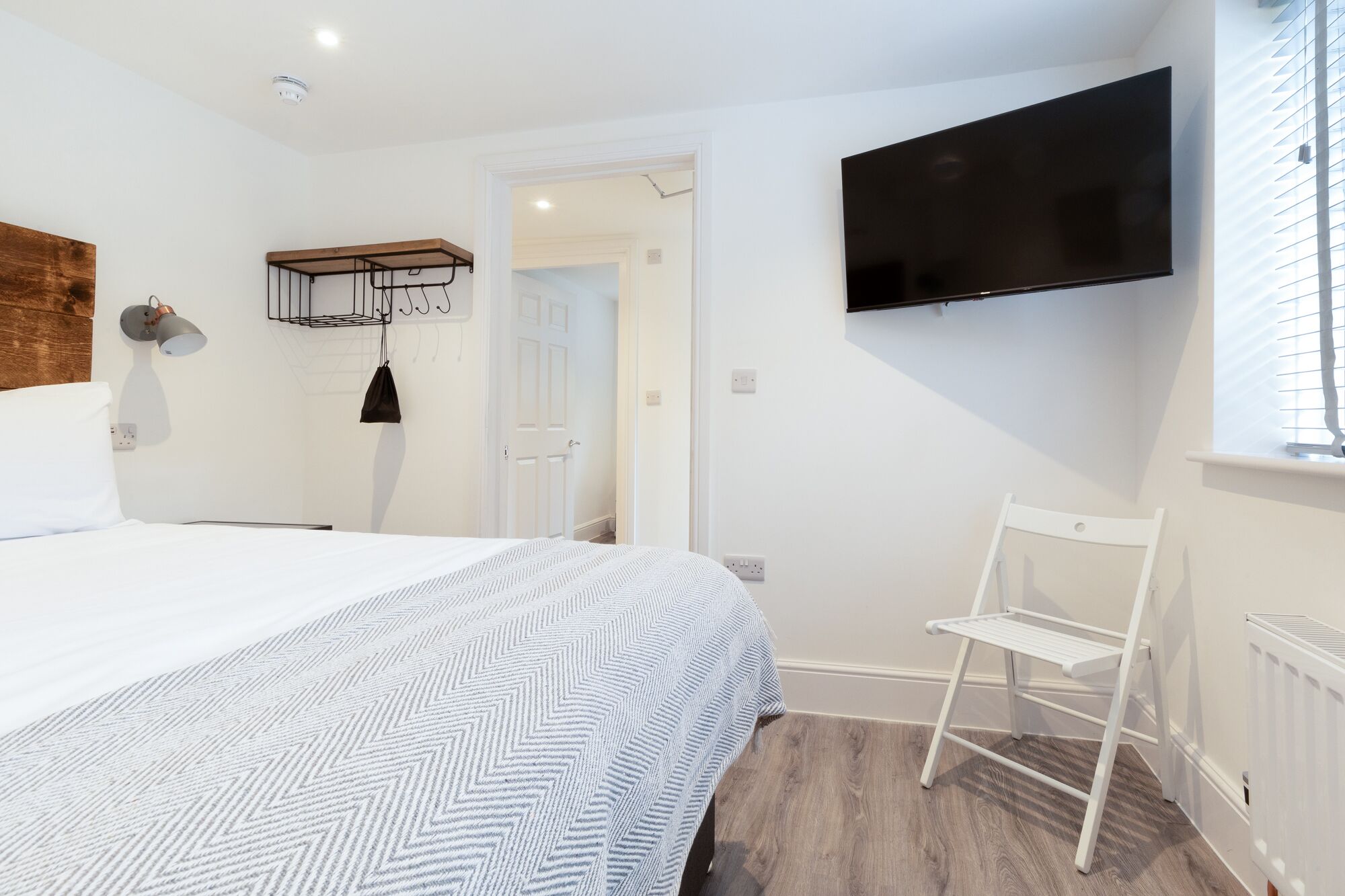 Une chambre d’hôtel moderne avec un grand lit, un téléviseur fixé au mur et une tête de lit en bois.