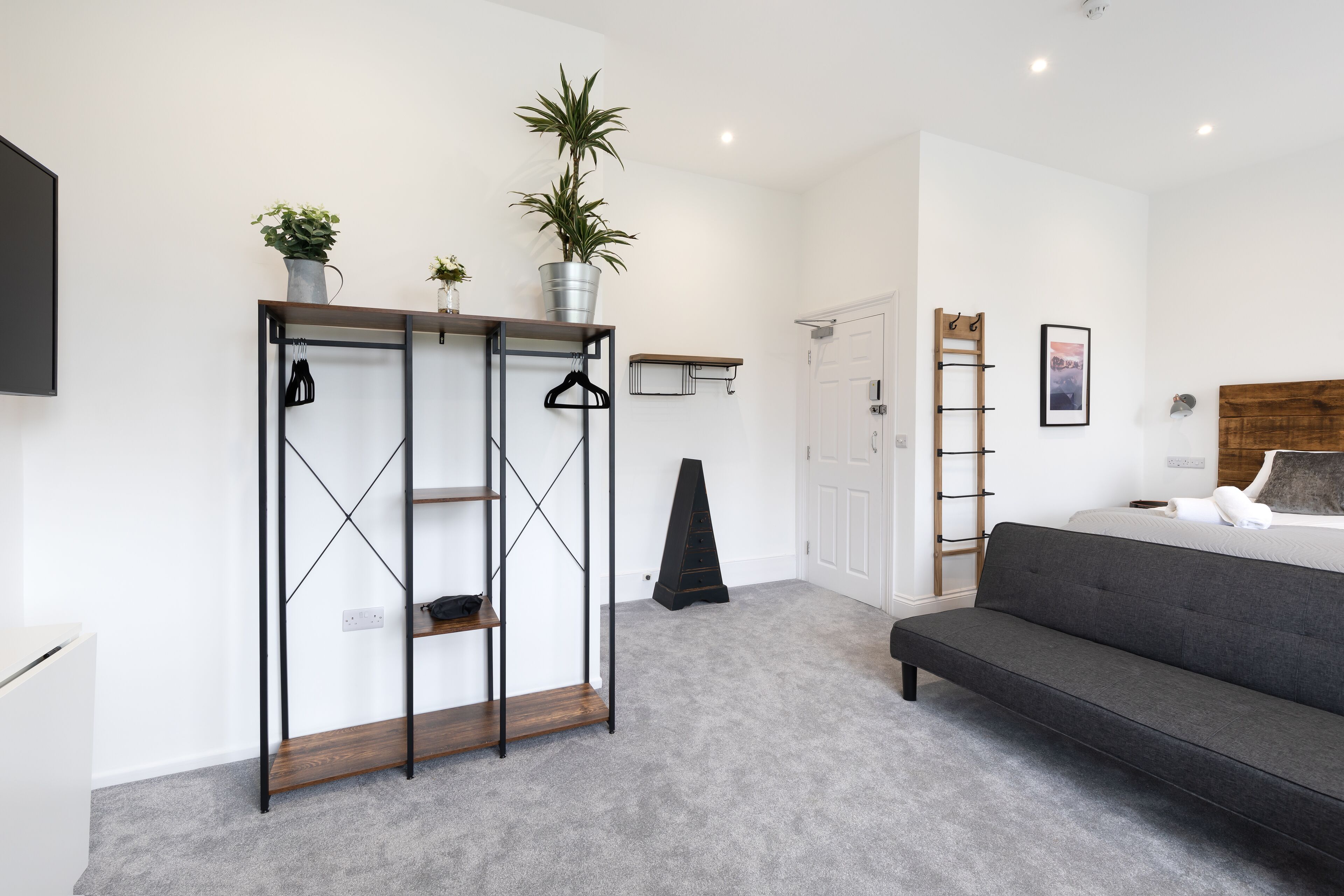 A modern bedroom with a grey sofa, a wardrobe with shelves, a bed, and a small desk.