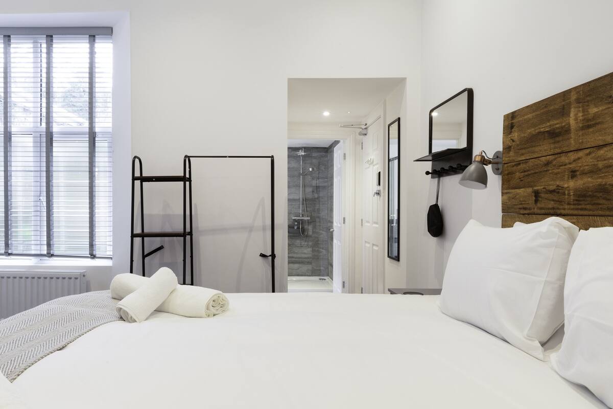 A modern hotel room with a large bed, a wooden headboard, a walk-in closet, and a shower area.