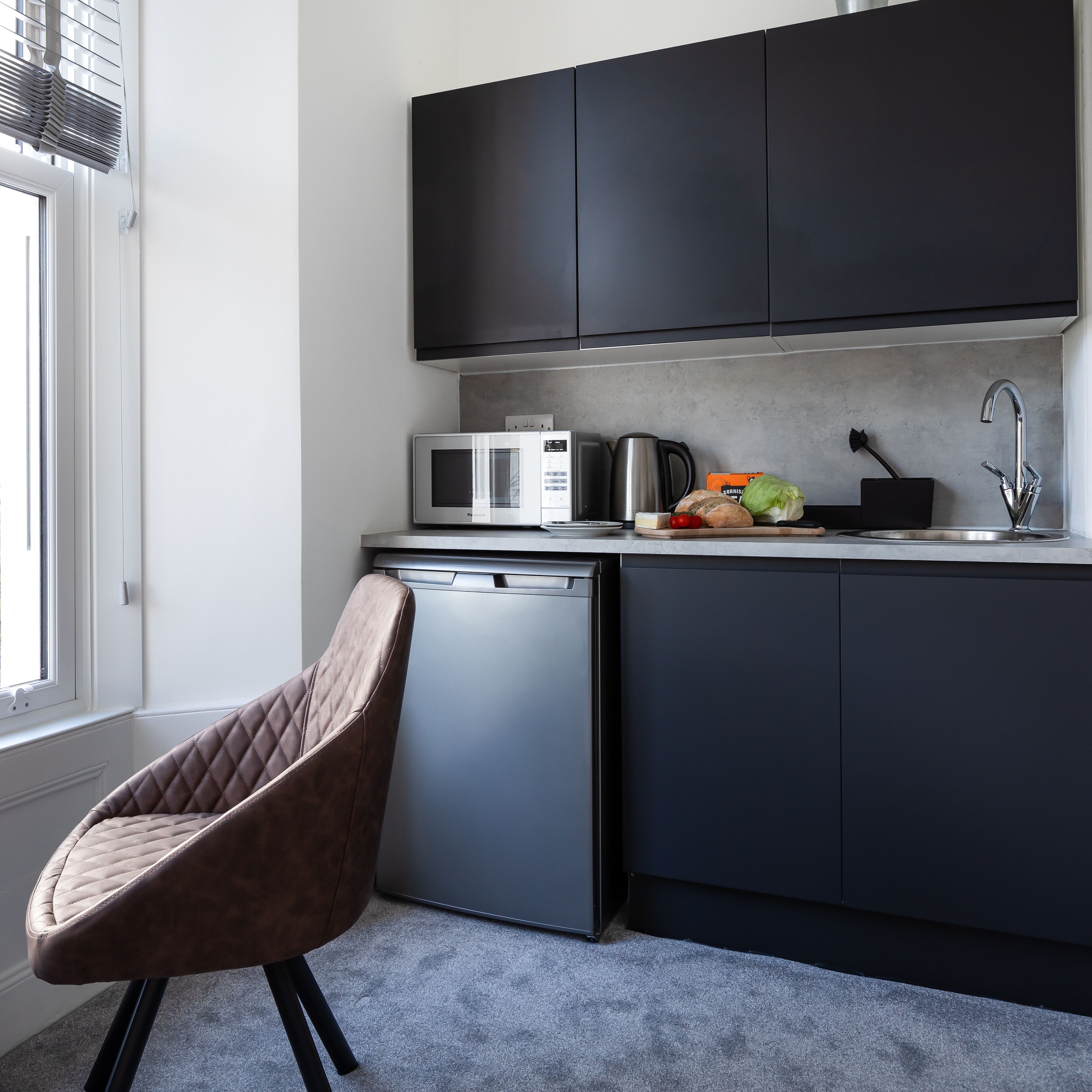 A modern kitchen with dark cabinets, a microwave, a coffee maker, and a sink.