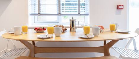 Una mesa de desayuno con una cafetera, platos, tazas y vasos de jugo de naranja.