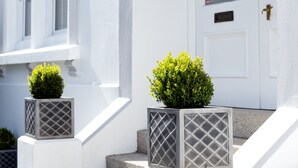 A white building with a door, windows, and a small garden with two potted plants. - Park View (Falmouth)