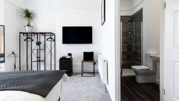 Un dormitorio moderno con cama, televisión, una mesita con una planta y un vestidor.