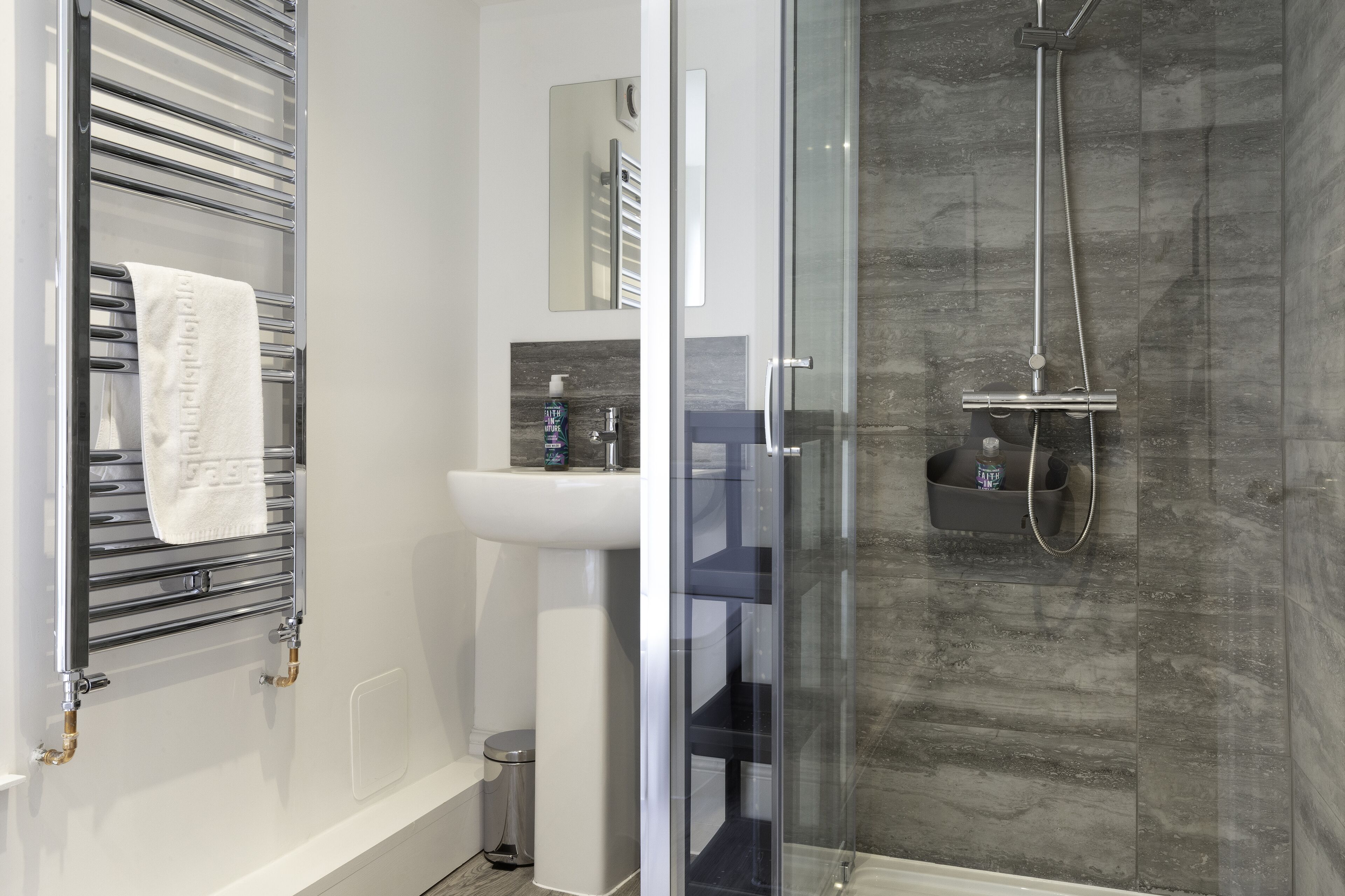 Un baño moderno con ducha de vidrio, un lavamanos blanco y un perchero para toallas.