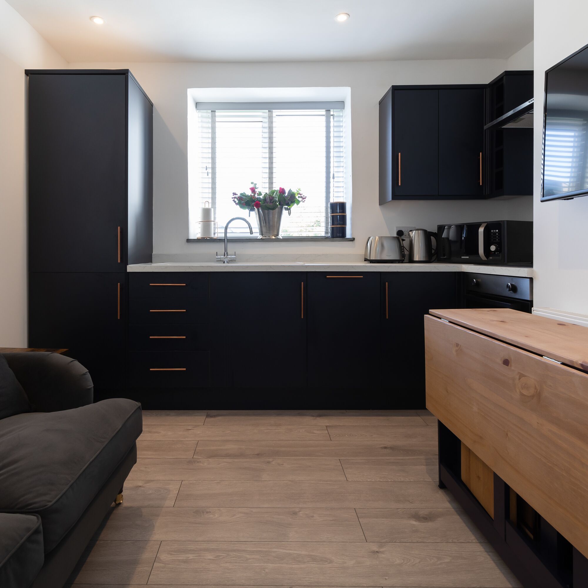 A modern kitchen with black cabinets, a wooden bench, and a window with blinds.