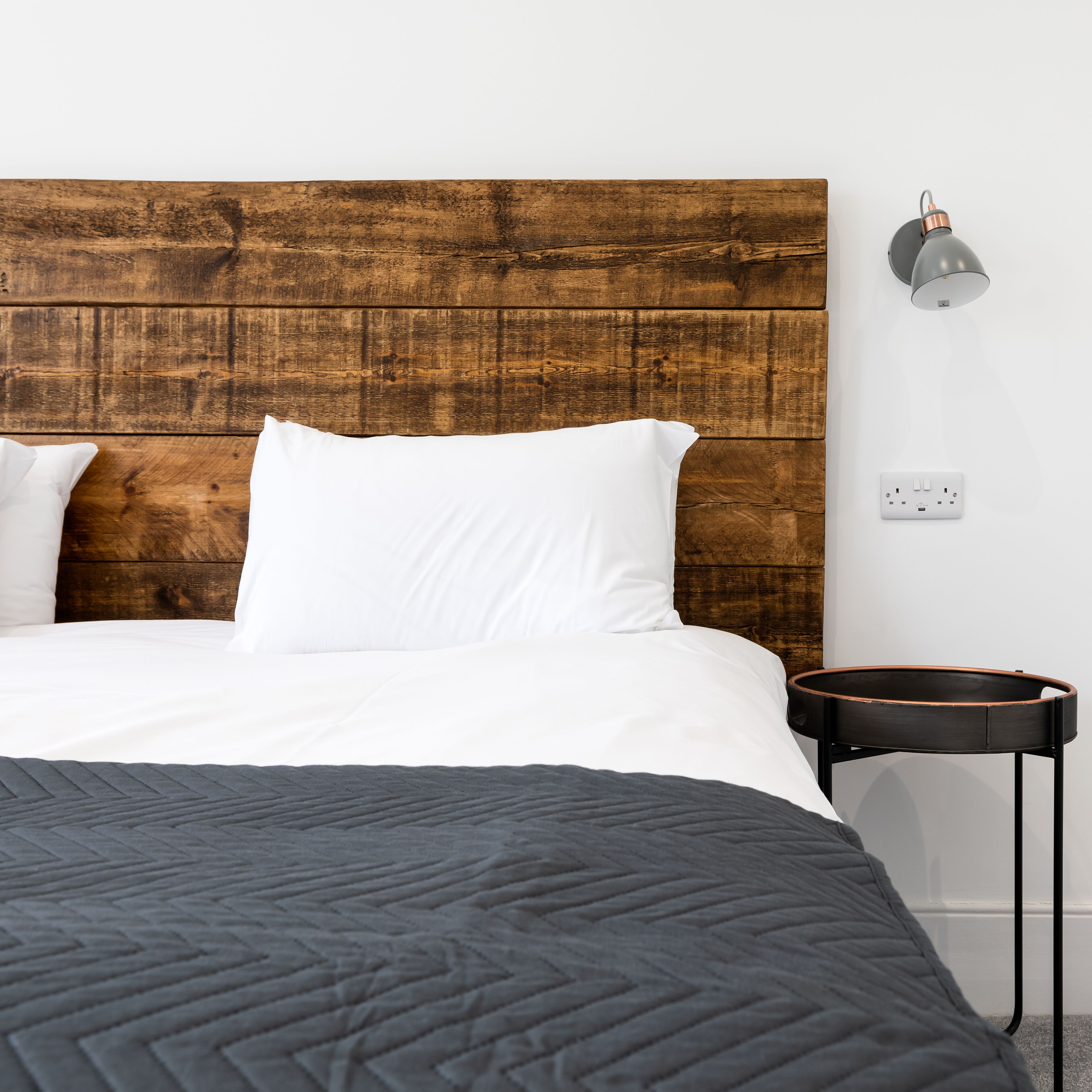 Een netjes opgemaakt bed met witte lakens en een donkere, gewatteerde spreidekker.