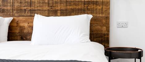 Een netjes opgemaakt bed met witte lakens en een donkere, gewatteerde spreidekker.