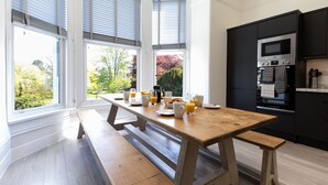 A modern kitchen with a wooden table set for breakfast, large windows, and black cabinetry. - Park View (Falmouth)