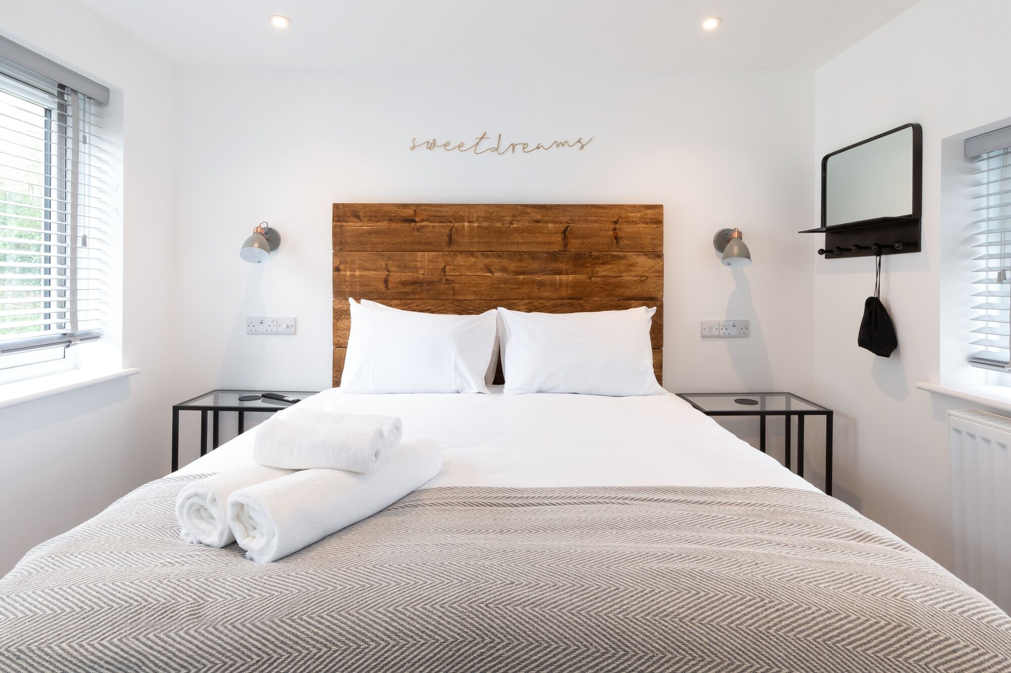 Ein modernes Hotelzimmer mit einem Holz-Kopfteil, weißer Bettwäsche und einem Nachttisch mit Lampe.