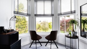 A corner room with a bay window, two chairs, a small table, and a radiator. - Park View (Falmouth)
