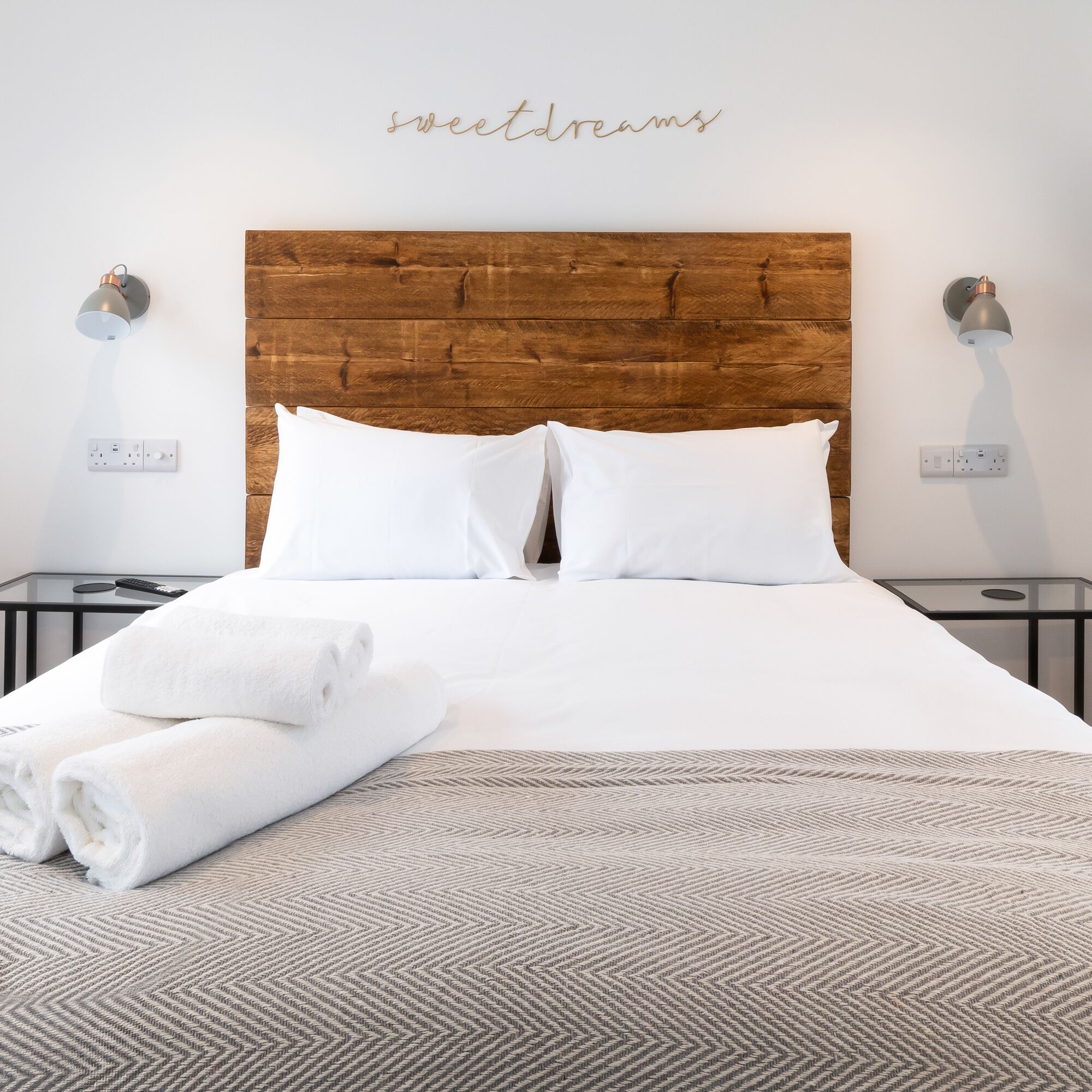 Una cama bien hecha con sábanas blancas, un cabecero de madera y una alfombra con motivos geométricos.