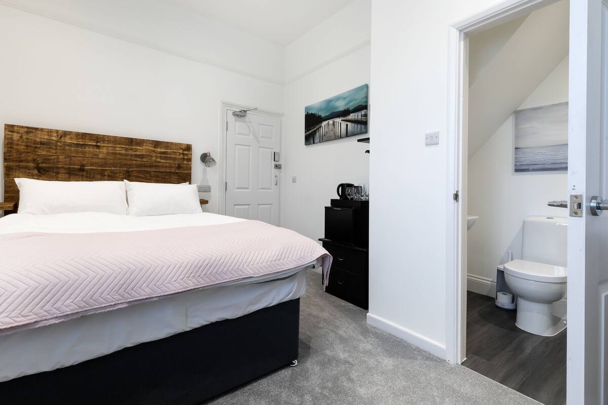 A bedroom with a bed, a door, a painting, and a bathroom with a toilet.