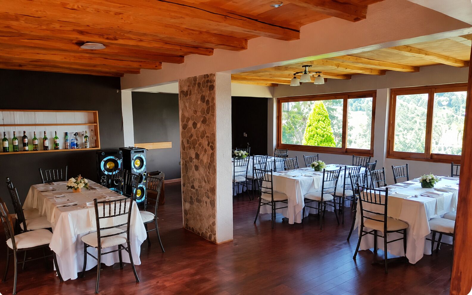 Ein Restaurant mit mehreren Essplätzen, einer Steinsäule und einer Holzbalkendecke.