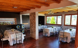 A restaurant with multiple tables set for dining, a stone pillar, and a wooden ceiling.