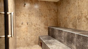 Ein Badezimmer mit beigen Fliesen, einer Duschkabine und einer Sitzbank.