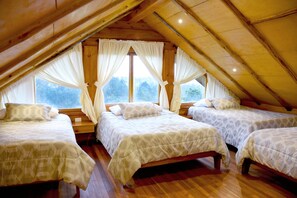 Habitación con tres camas dispuestas en fila, suelo de madera y techo inclinado con ventanas.
