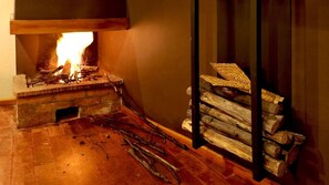 Ein Kamin mit brennenden Holzscheiten, ein Holzboden und ein Holzstapel an einer Wand.