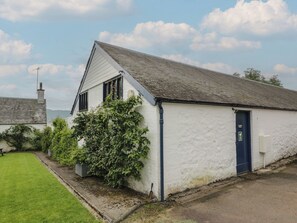 A white building with a dark blue door, a small garden, and a clear sky. - Fordie Lodge (Crieff)
