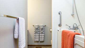 Un baño con una bañera blanca, una ducha con cabezal de ducha manual y dos toallas colgadas en un perchero.