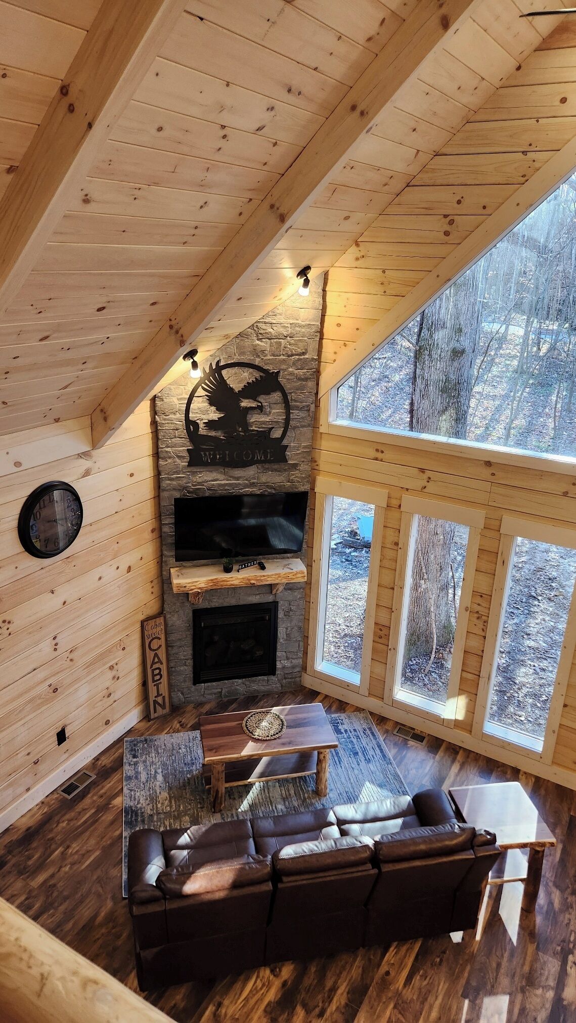 Een knus interieur van een blokhut met een stenen openhaard, houten wanden, een leren bank en een groot raam met uitzicht op het bos.