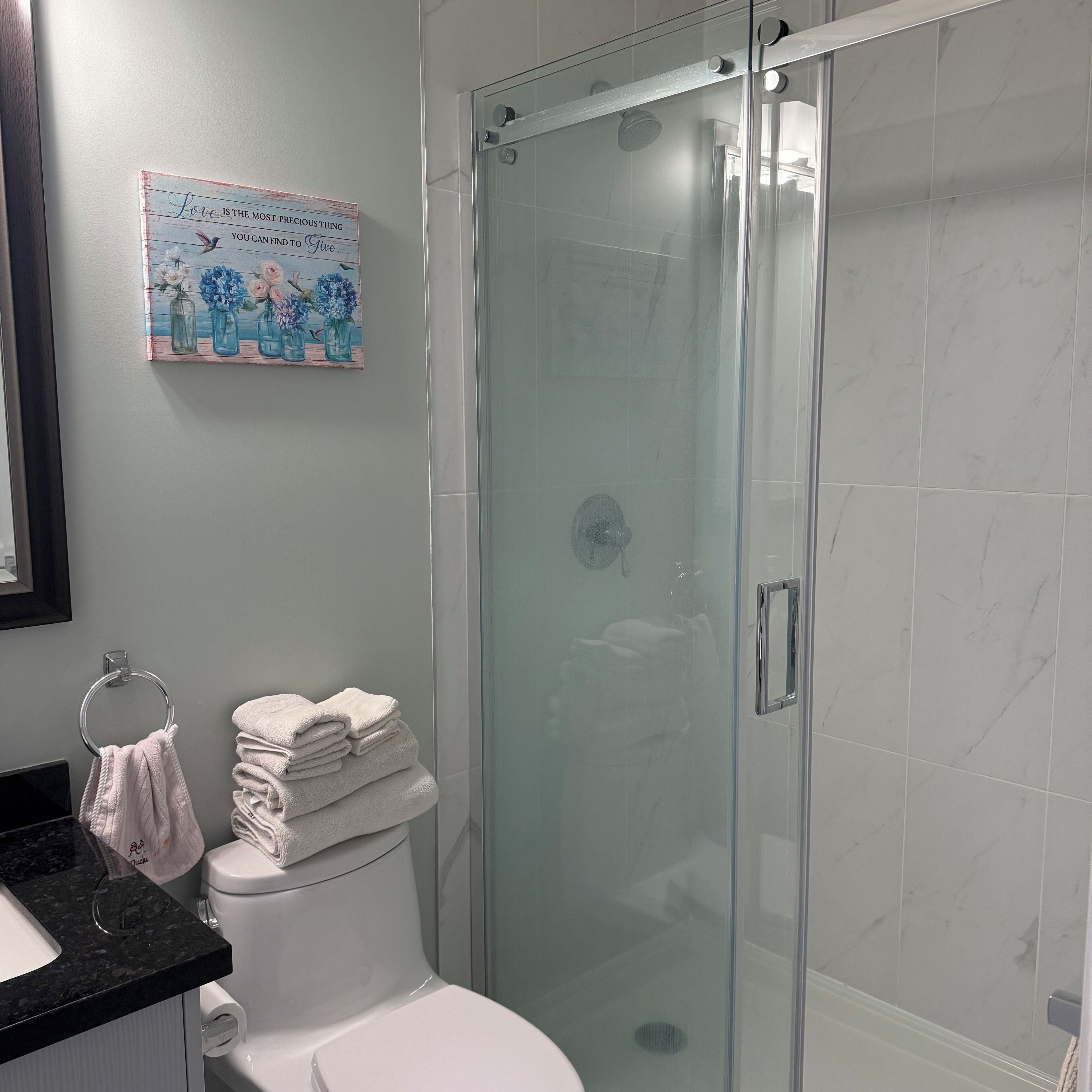 A bathroom with a glass-enclosed shower, a toilet, and a sink with a black countertop.