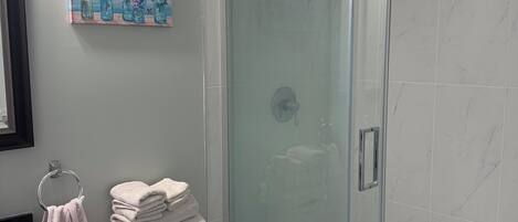 A bathroom with a glass-enclosed shower, a toilet, and a sink with a black countertop.