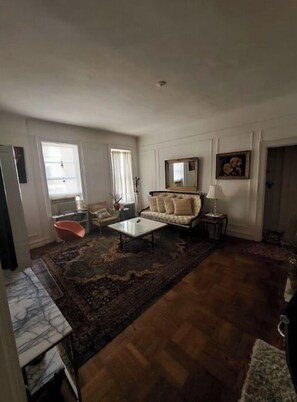 Relax in this spacious living room with a high ceiling and large window, featuring a comfortable sofa, coffee table, and patterned rug.