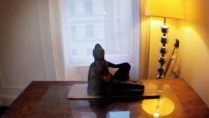 Una habitación con una mesa, una lámpara y una ventana que da a edificios.