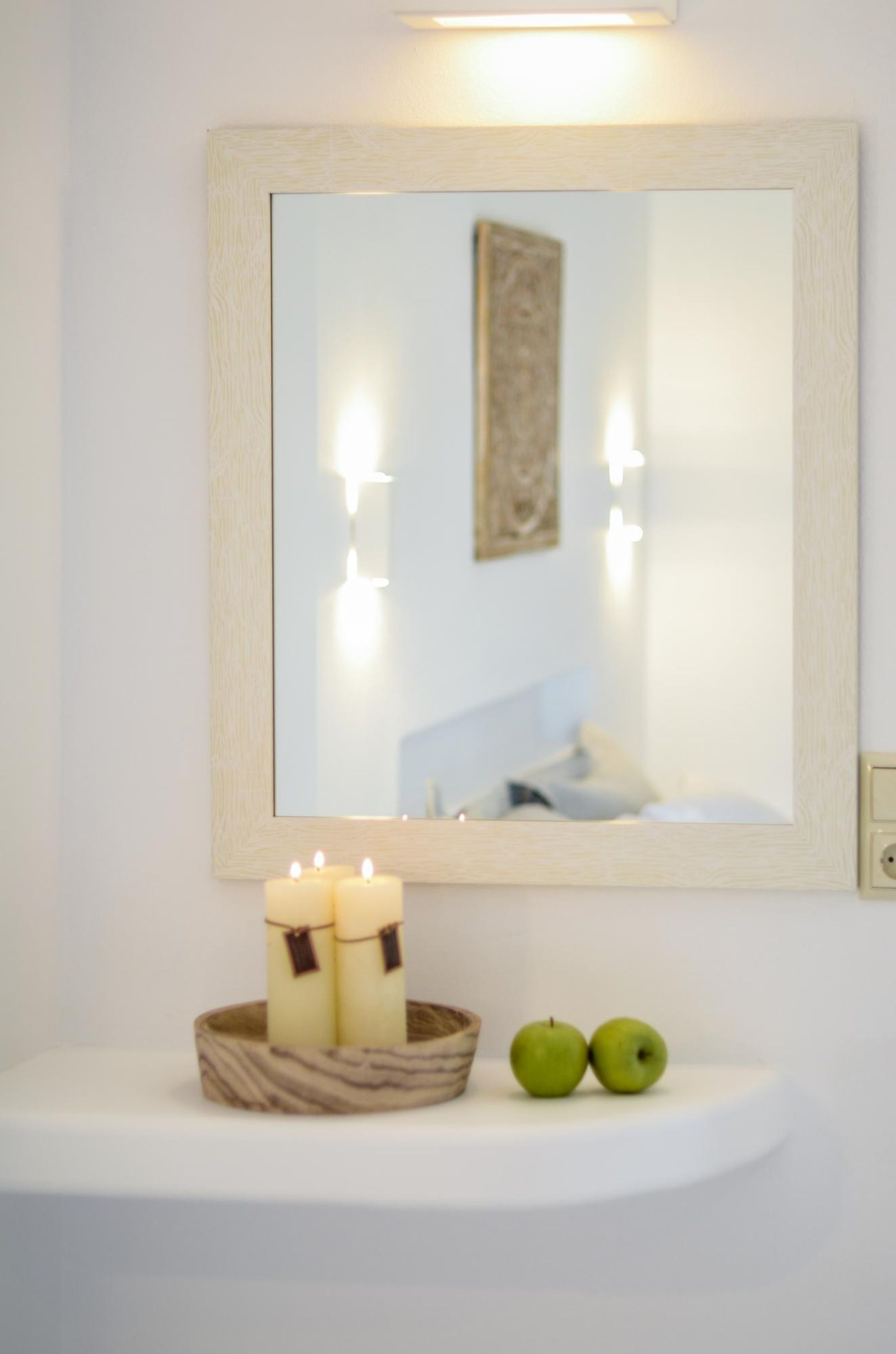 A bathroom vanity with a mirror, candles, and apples.