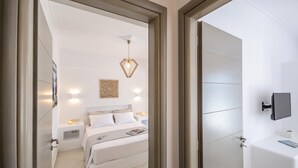 A modern bedroom with a bed, bedside tables, a wall-mounted TV, and a geometric pendant light. - Rocks Naxian Villa With Private Pool (Naxos)