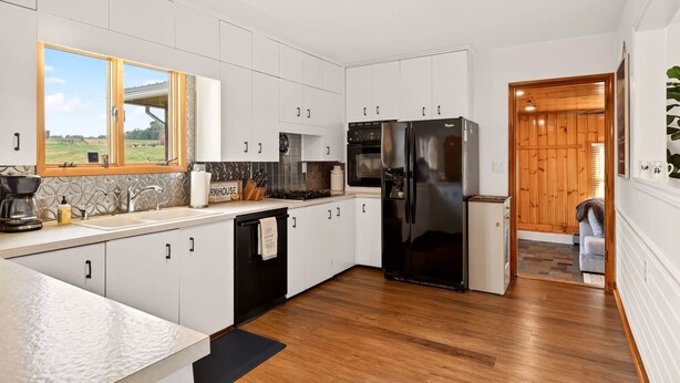 A modern kitchen with white cabinets, a black refrigerator, and a wooden floor.