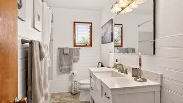 A bathroom with a white vanity, a toilet, a shower area, and a window with blinds.